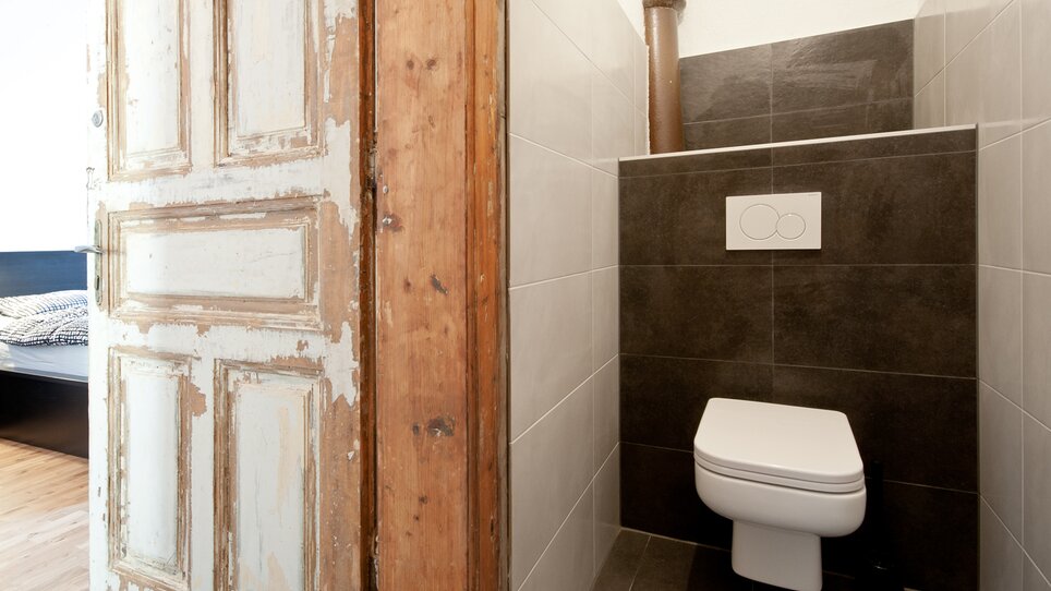 Vista interna di un bagno con WC e porta in legno. | © Grocholl