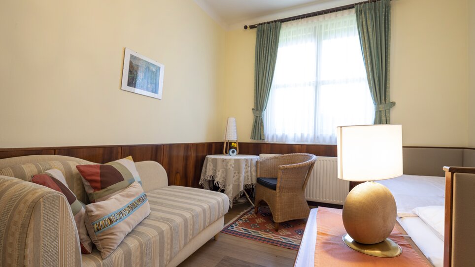 Area soggiorno con divano, tavolo e finestra in Haus Anna. | © Haus Anna – Apartments im Garten