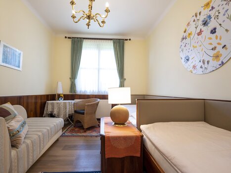 Bright room with sofa, table, and window, decorated with floral motif. | © Haus Anna – Apartments im Garten