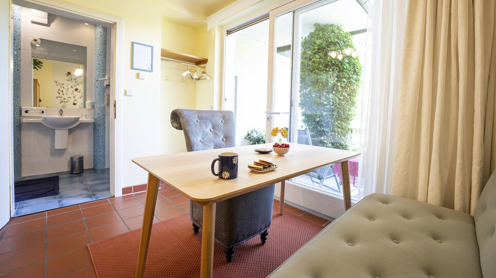 Un interno con tavolo, sedie e vista su un giardino. | © Haus Anna – Apartments im Garten