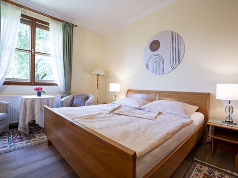 A bright bedroom with two windows, wooden beds, and modern wall art. | © Haus Anna – Apartments im Garten