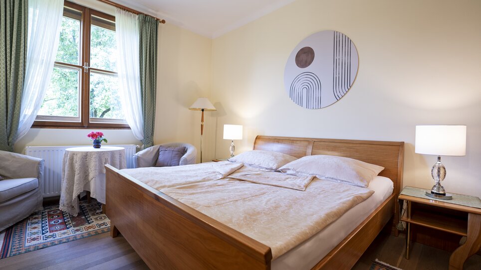 Una camera da letto luminosa con due finestre, letti in legno e arte moderna. | © Haus Anna – Apartments im Garten