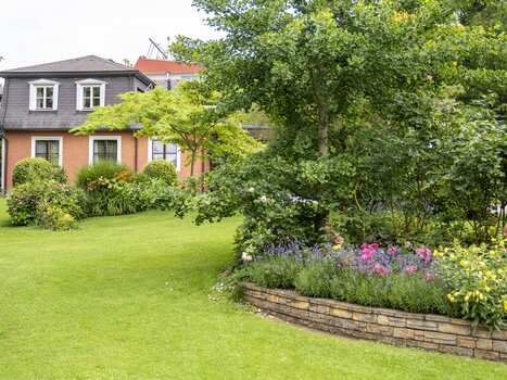Garden with flower bed and Haus Anna in the background. | © Haus Anna – Apartments im Garten