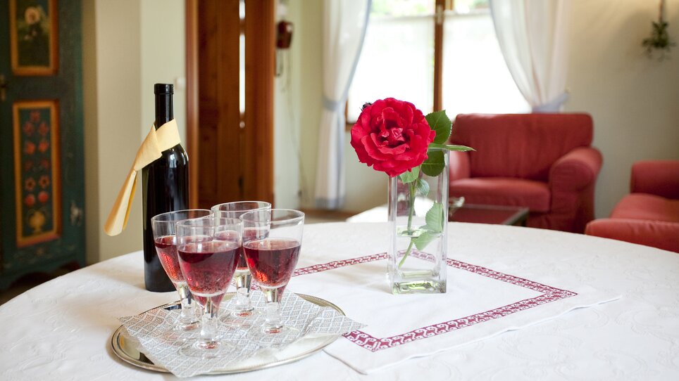Tavolo con bicchieri pieni di succo d'uva e una rosa in un bicchiere. | © Haus Anna – Apartments im Garten