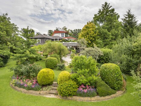 View of the garden with various plants and a house. | © Haus Anna – Apartments im Garten