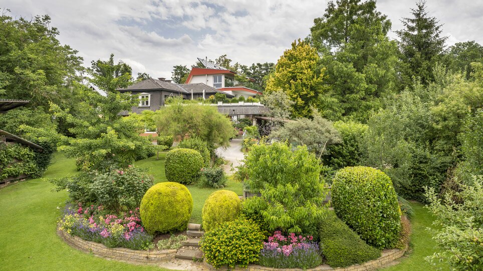 Vista del giardino con diverse piante e una casa. | © Haus Anna – Apartments im Garten