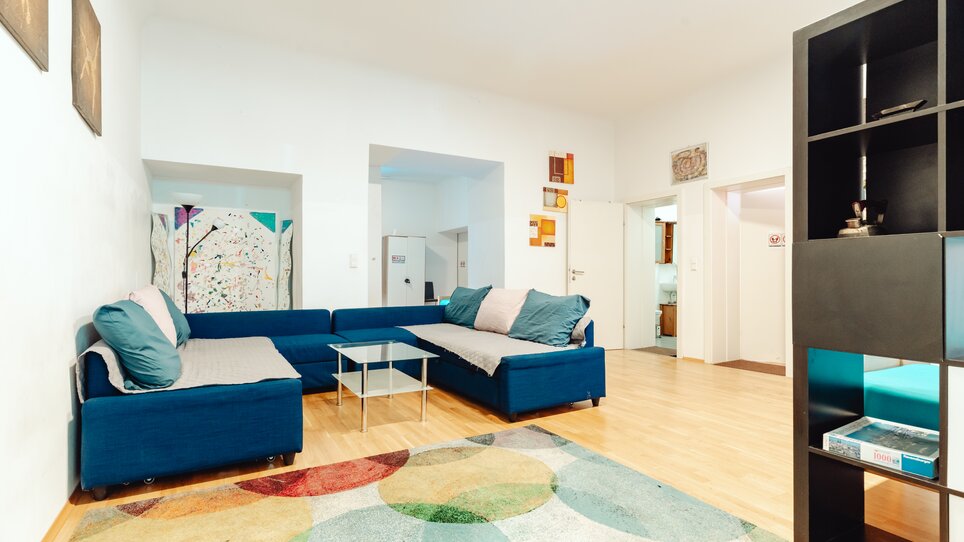 Ein modernes Wohnzimmer mit blauem Sofa, Glastisch und buntem Teppich. | © Lilians Apartments