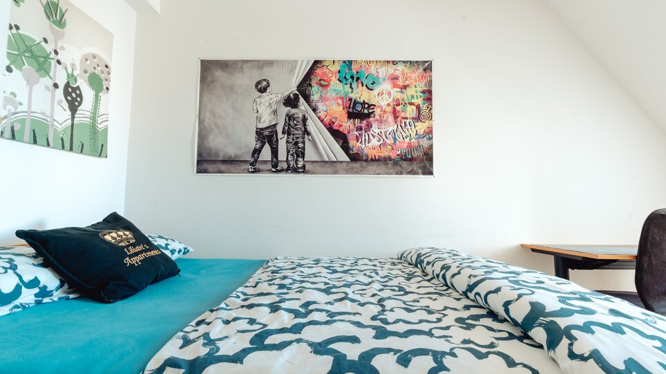 Ein Zimmer mit Doppelbett und einem Wandbild von zwei Kindern. | © Lilians Apartments