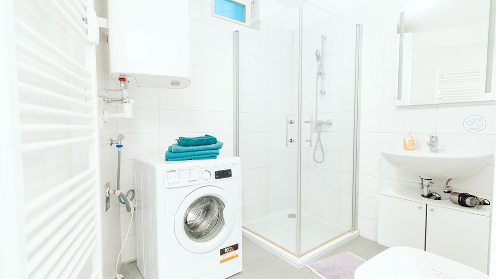 Modernes Badezimmer mit Dusche, Waschmaschine und Handtüchern. | © Lilians Apartments