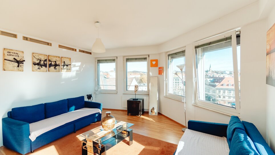 Gemütlicher Wohnraum in Graz mit blauen Sofas und großem Fensterblick. | © Lilians Apartments