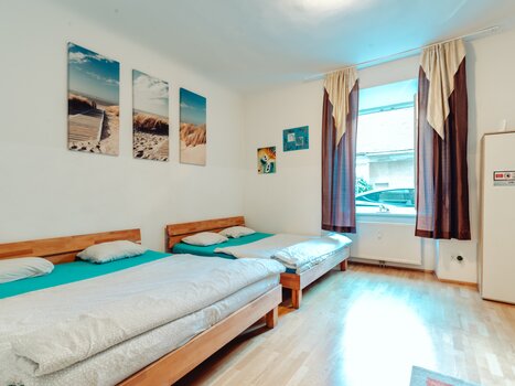 Helles Zimmer mit zwei Doppelbetten, Fenster und Bildern an der Wand. | © Lilians Apartments
