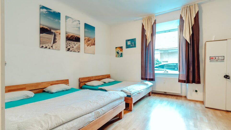 Helles Zimmer mit zwei Doppelbetten, Fenster und Bildern an der Wand. | © Lilians Apartments