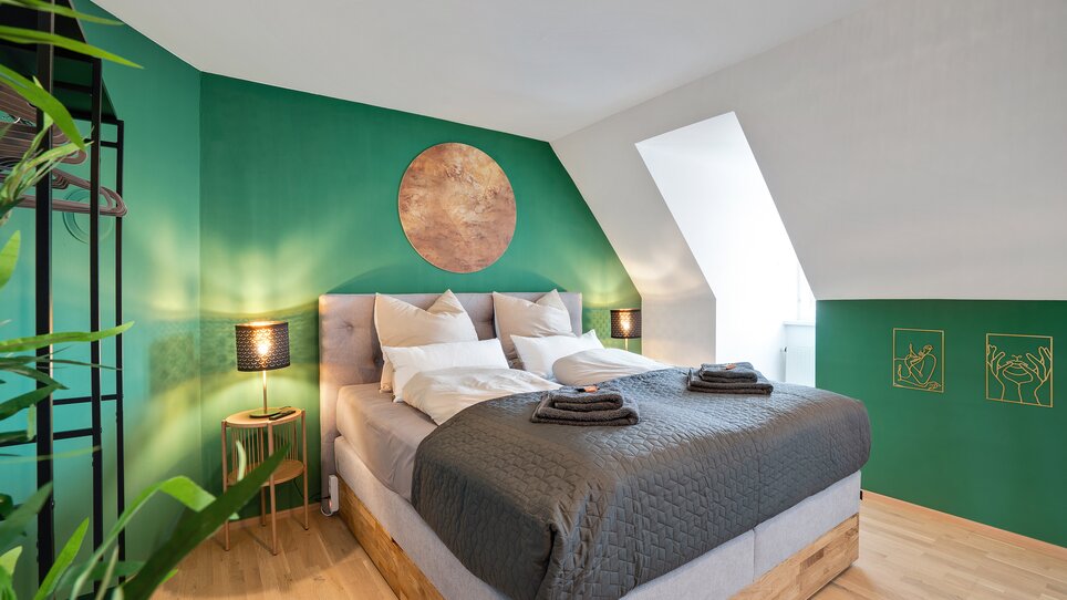 Modernes Schlafzimmer mit Doppelbett und grünen Wänden. | © HERO HOMES Design Apartments