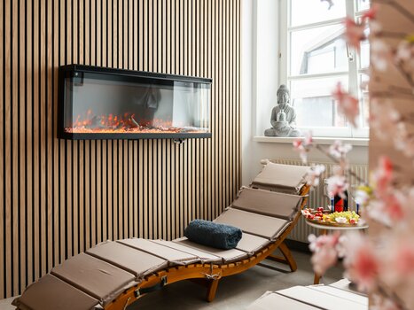 Modern spa room with lounge chair, electric fireplace, and Buddha statue. | © HERO HOMES Design Apartments