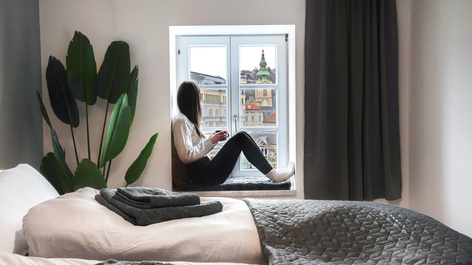 Eine Person sitzt am Fenster und genießt den Blick auf Graz. | © HERO HOMES Design Apartments