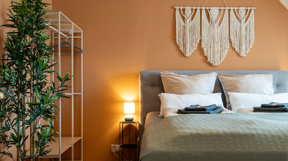 Elegantes Schlafzimmer mit Kleiderständer, Makramee-Dekor und sanfter Beleuchtung. | © HERO HOMES Design Apartments