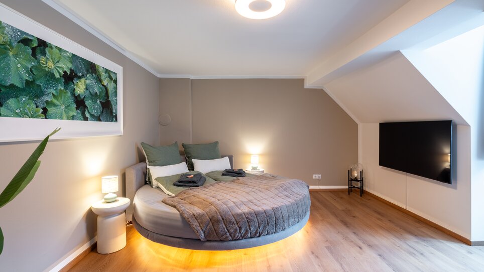Elegantes Schlafzimmer mit rundem Bett und Fernseher. | © HERO HOMES Design Apartments