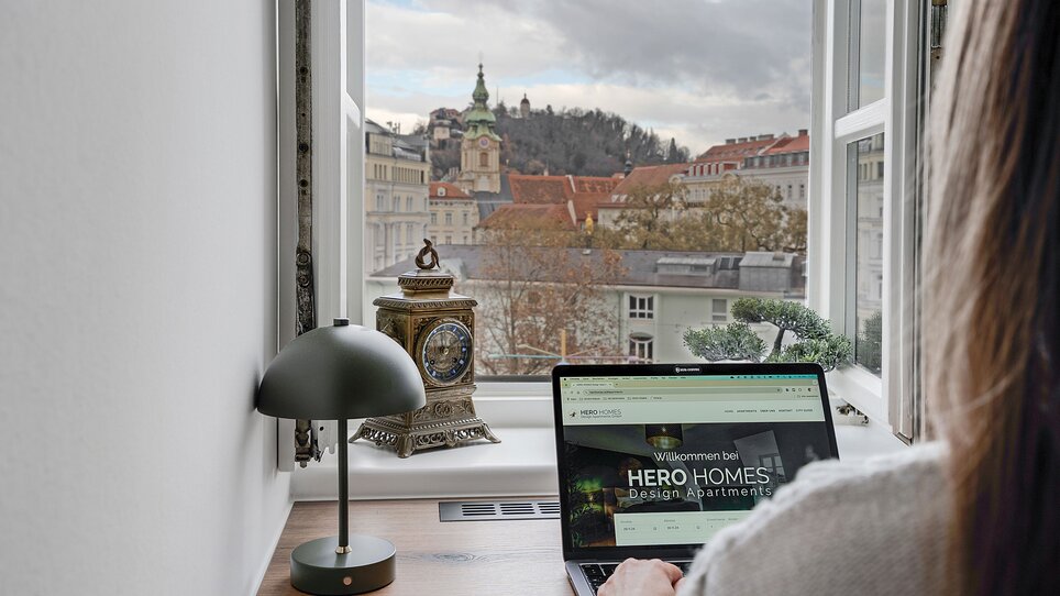 Gemütliches Arbeitsumfeld mit Laptop und Blick auf Graz. | © -HERO-HOMES-Design-Apartments_2