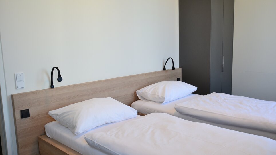 Due letti singoli in una stanza luminosa con armadio. | © Tomo-Tec Immo GmbH