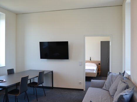 A view of TT-Rooms Apartment-Hotel featuring a table, TV, and access to a bedroom. | © Tomo-Tec Immo GmbH