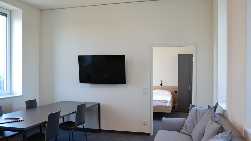 Una vista del TT-Rooms Apartment-Hotel con tavolo, TV e accesso a una camera da letto. | © Tomo-Tec Immo GmbH
