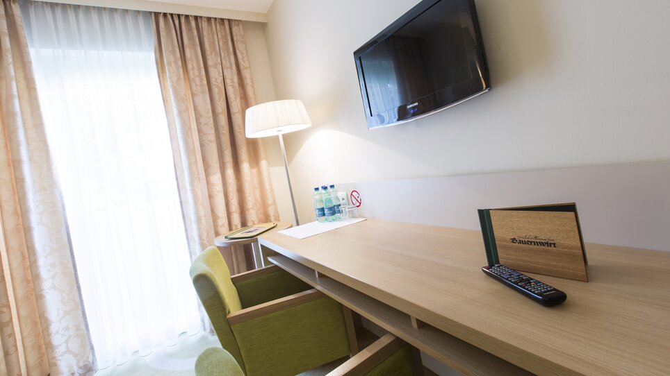 Gemütliches Hotelzimmer mit Schreibtisch, TV und Blick auf die Fenster. | © Bauernwirt