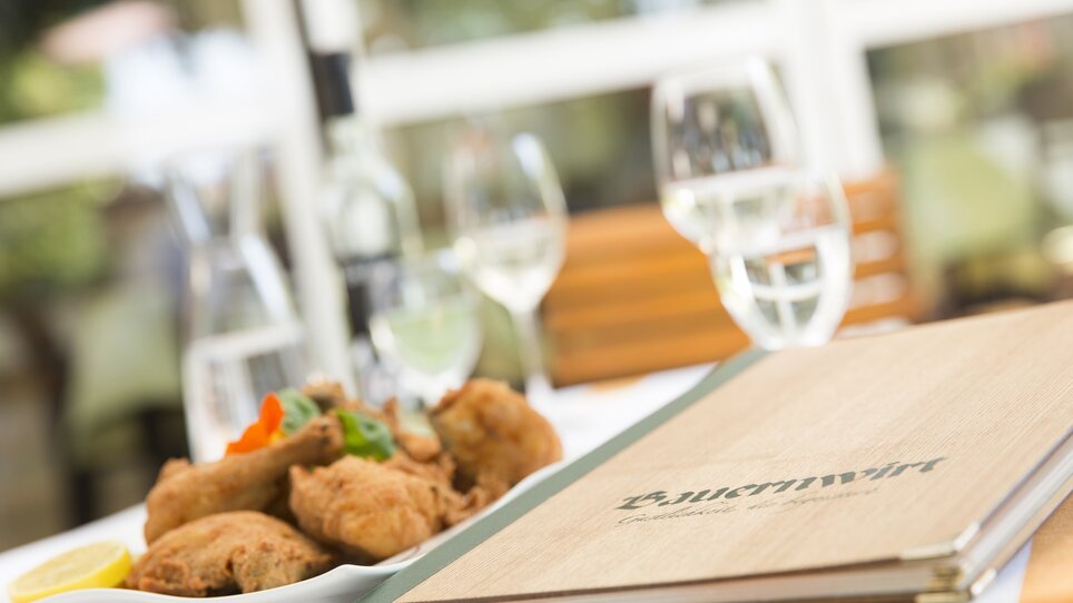 Ein gedeckter Tisch mit einer Speisekarte und einem Teller mit Backhendl. | © Bauernwirt