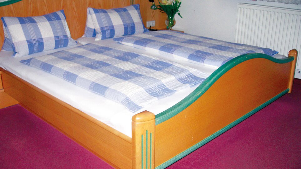 Una camera con un letto matrimoniale, coperte e cuscini a quadretti. | © Schmiedwirt