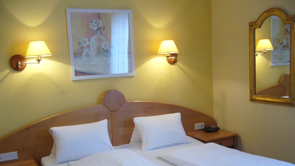 Camera con due letti, comodini e specchio a parete. | © Legenstein
