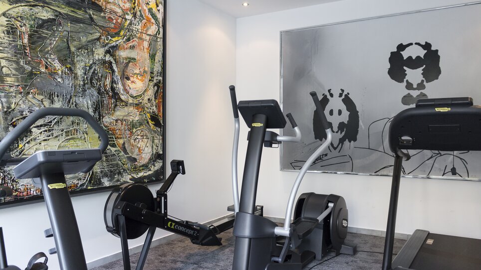 Fitnessraum mit Geräten und modernen Kunstwerken an der Wand. | © Augarten Art Hotel