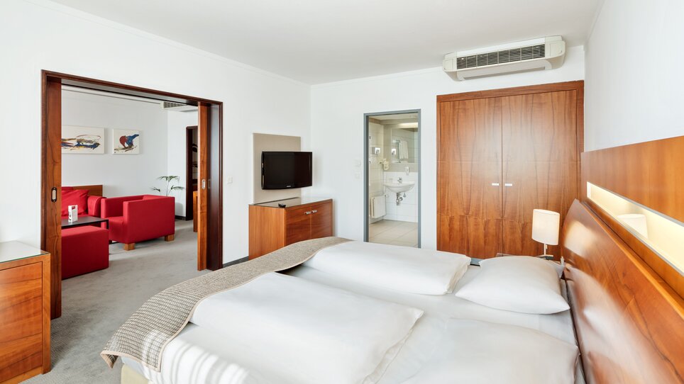 Einblick in ein Hotelzimmer mit Doppelbett und angrenzendem Wohnbereich. | © Austria Trend Hotel Europa