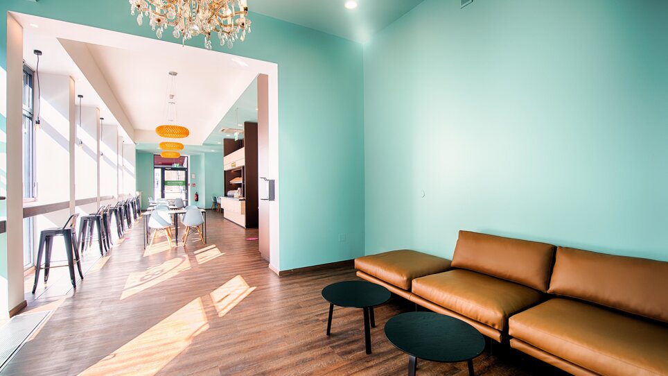Heller Loungebereich mit türkisen Wänden und braunem Sofa. | © B&B Hotels 2023
