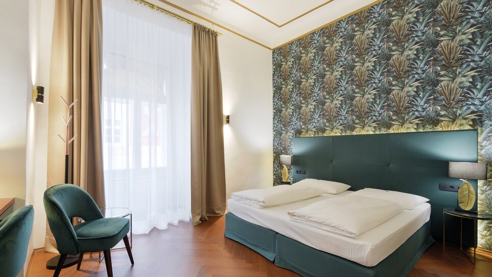 Ein stilvolles Schlafzimmer mit hellem Farbdesign und Pflanzenmuster an der Wand. | © Hotelpartner