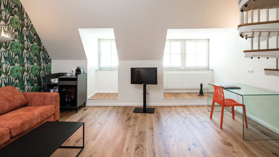 Heller Wohnbereich mit Sofa, TV und Schreibtisch im Dachgeschoss. | © Robert Illemann