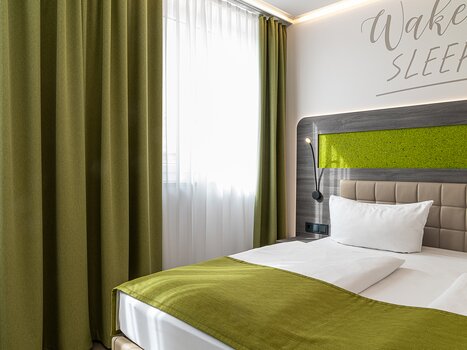 A room with a bed, green curtains, and wall decoration. | © Chrizz Rooms