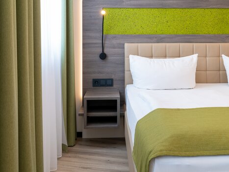 View of a bedroom with bed, nightstand, and curtains in green tones. | © Chrizz Rooms