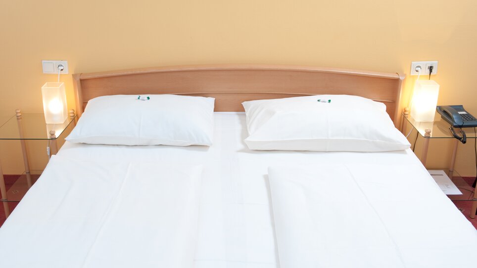 A double bed with two white pillows and nightstands. | © Feichtinger