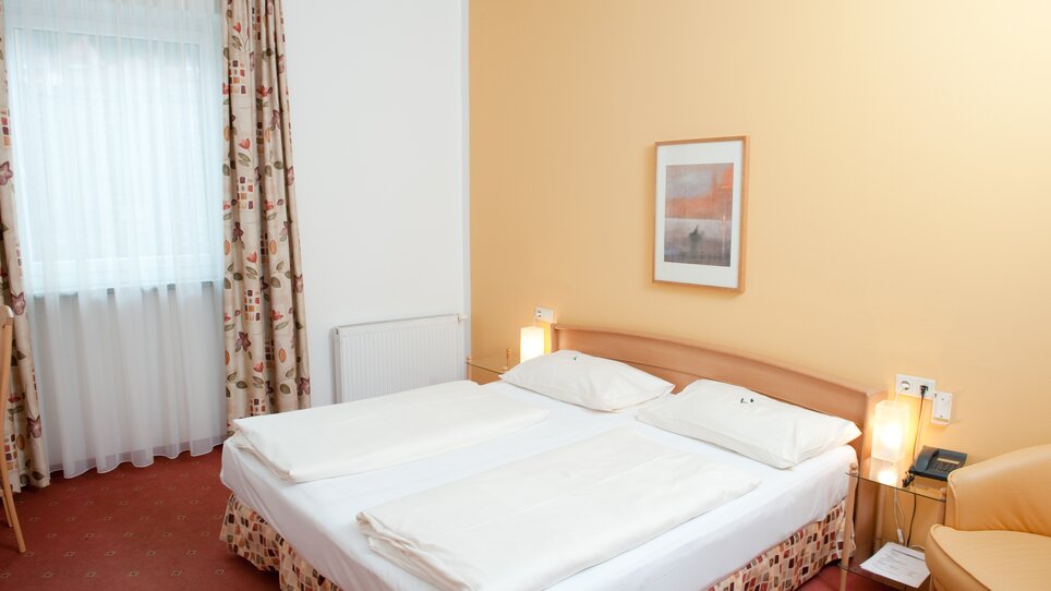 A simple hotel room with two beds and a window. | © Feichtinger