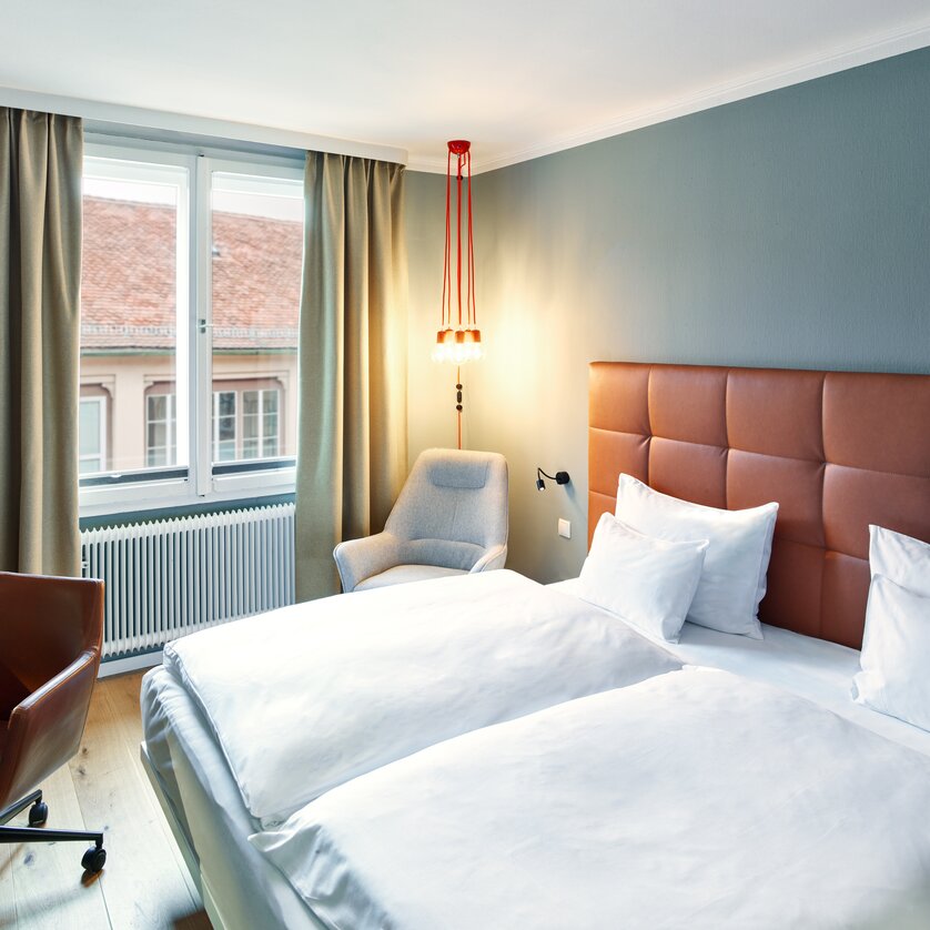 Bright hotel room featuring two beds and a seating area.
