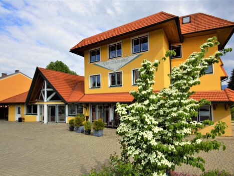 The image shows a charming yellow building with a red roof and blooming plants. | © Der Marienhof