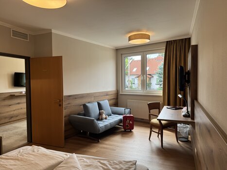 Spacious hotel room featuring a sofa, desk, and TV. | © Der Marienhof