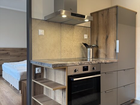 Compact kitchen area featuring an oven, extractor hood, and wood shelving. | © Der Marienhof