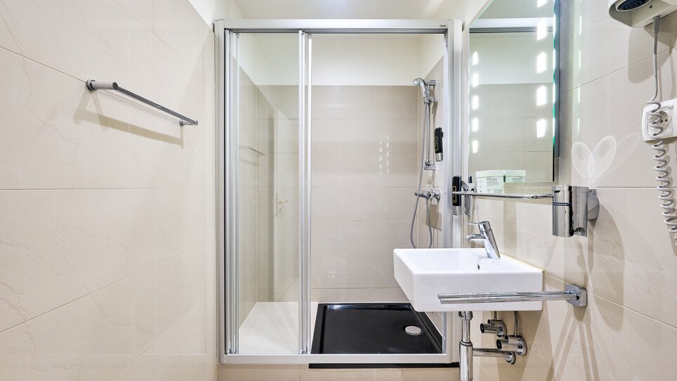 Badezimmer mit Dusche, Waschbecken und heller Beleuchtung. | © EKONO by Leva Hotel Strasser