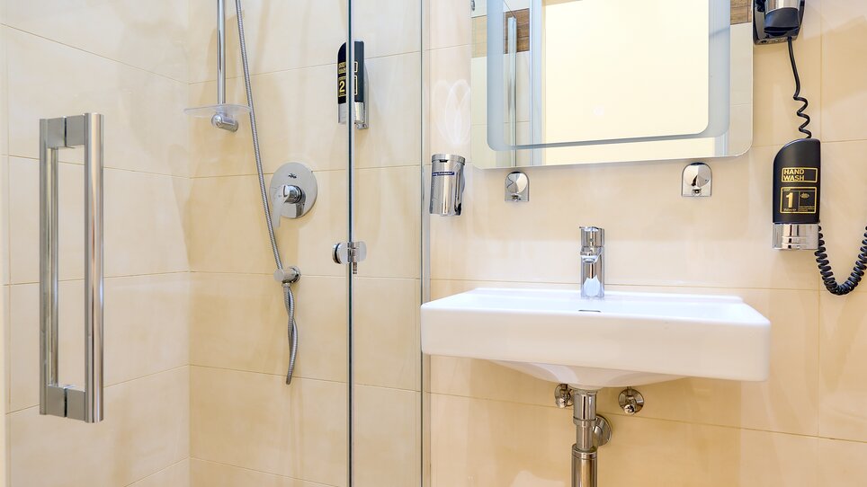 Ein Badezimmer mit Duschbereich, Waschbecken und Spiegel, ausgestattet mit einem Fön. | © EKONO by Leva Hotel Strasser
