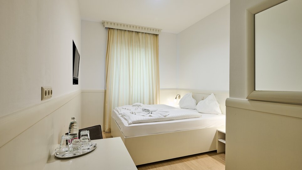 Ein Hotelzimmer mit einem Bett, einem TV und einem Tisch. | © EKONO by Leva Hotel Strasser