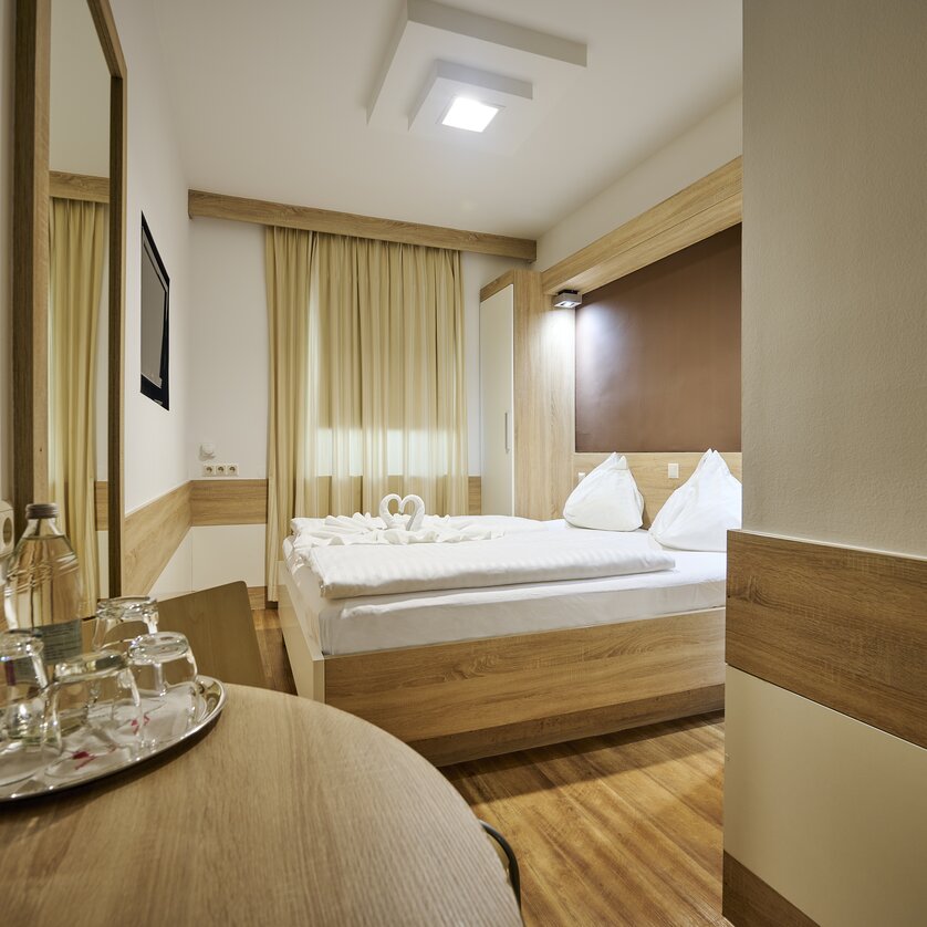 Ein helles Hotelzimmer mit Doppelbett und einem Spiegel. | © EKONO by Leva Hotel Strasser