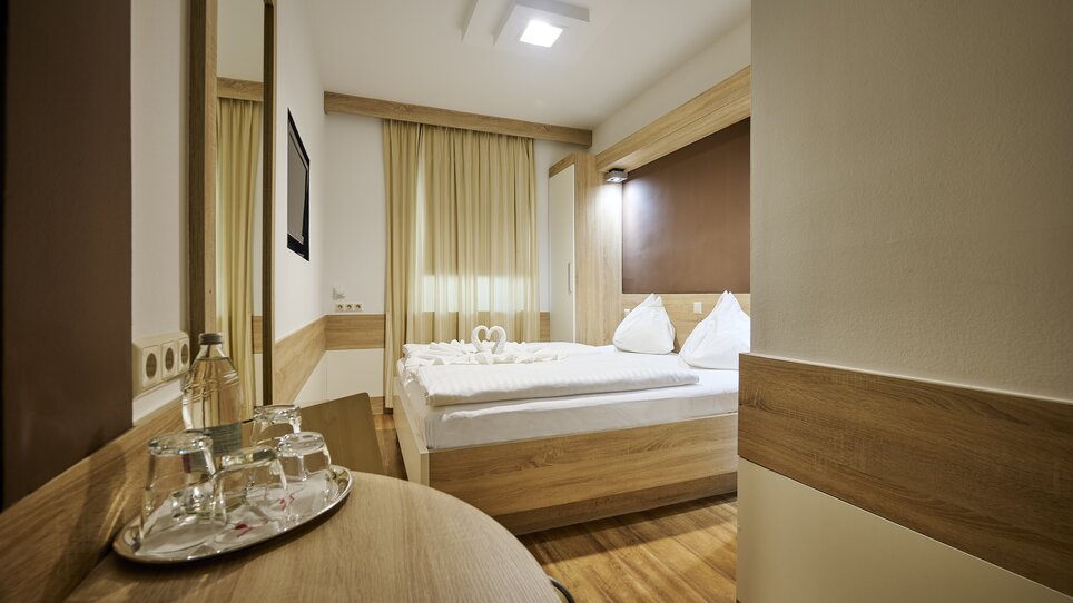 Ein helles Hotelzimmer mit Doppelbett und einem Spiegel. | © EKONO by Leva Hotel Strasser