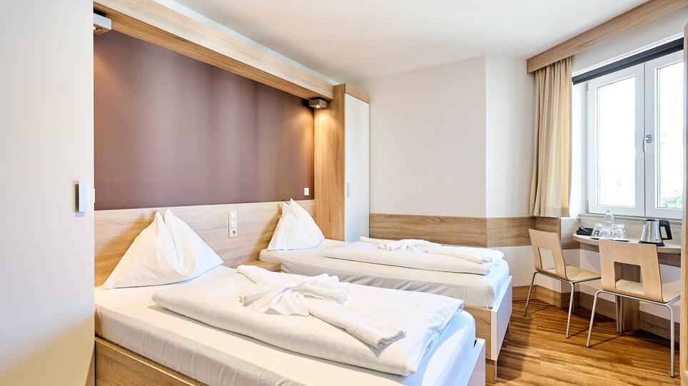 Helles Zimmer mit zwei Betten, Tisch und Fenster. | © EKONO by Leva Hotel Strasser