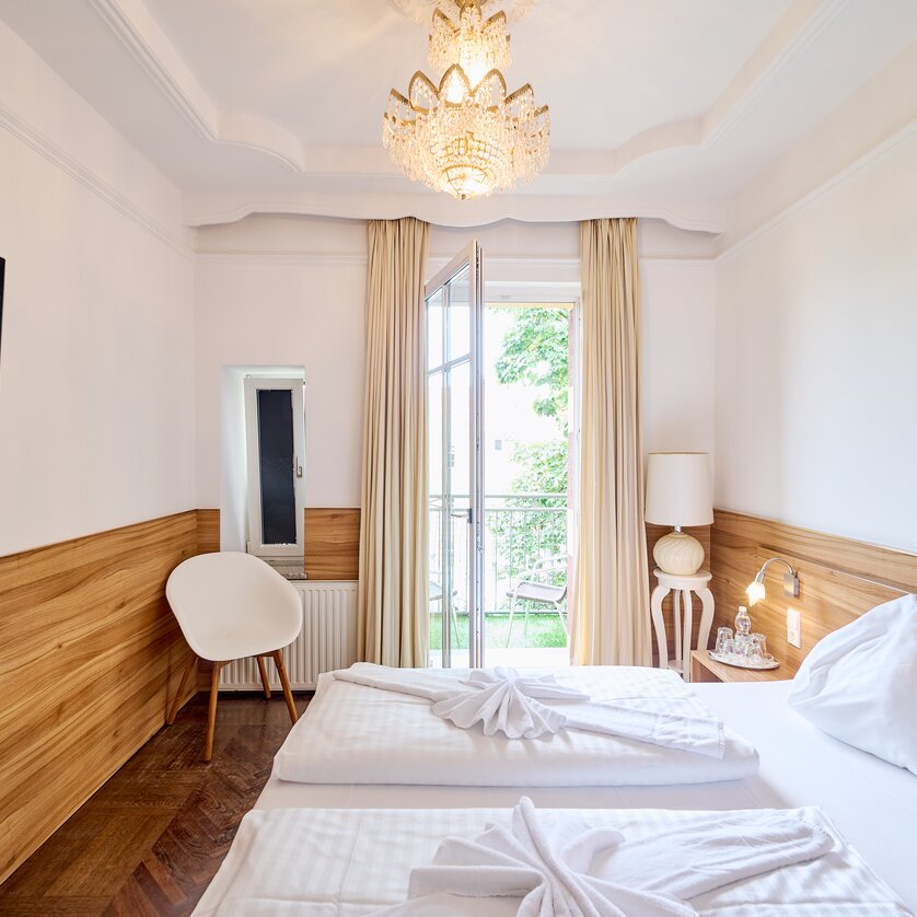 Bright hotel room with two beds, TV, and balcony. | © EKONO by Leva Hotel Strasser
