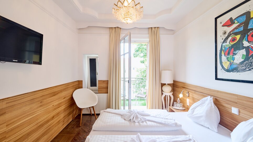Helles Hotelzimmer mit zwei Betten, Fernseher und Balkon. | © EKONO by Leva Hotel Strasser